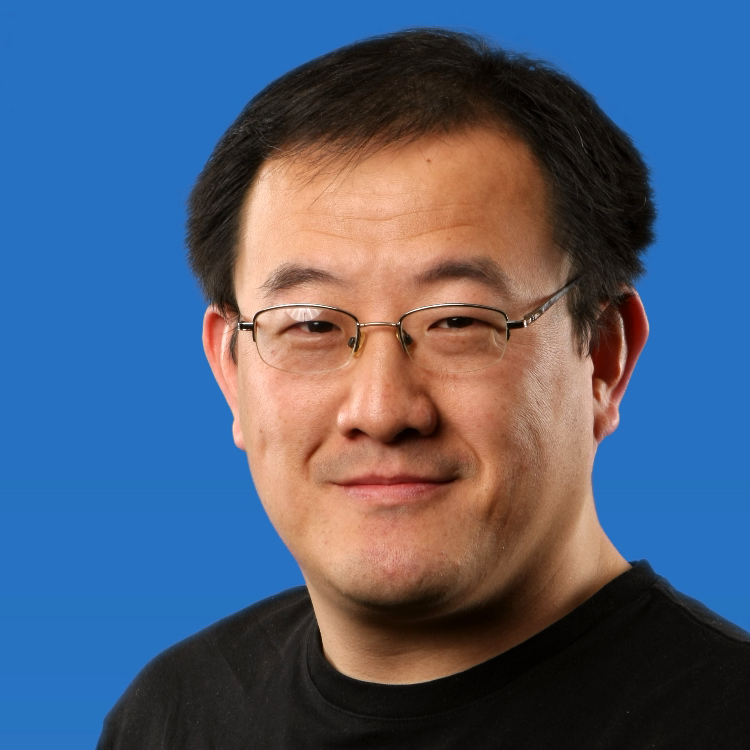 Man with glasses and black hair looking at the camera in front of a blue background