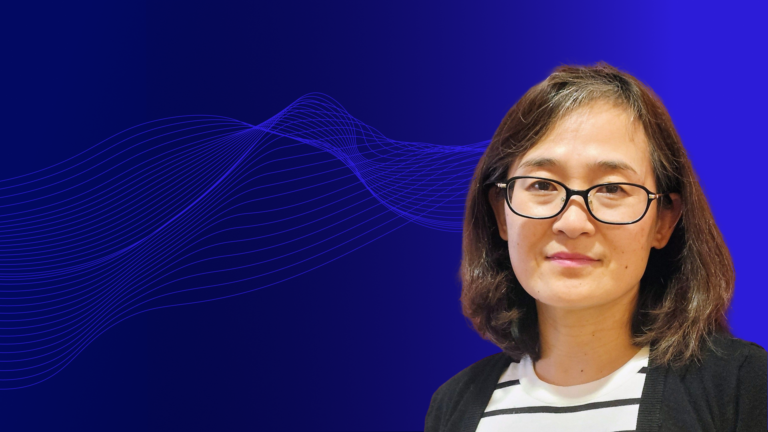 Portrait of a woman with shoulder-length dark hair and glasses, wearing a black cardigan over a white striped shirt, set against a blue gradient background with abstract wave lines.