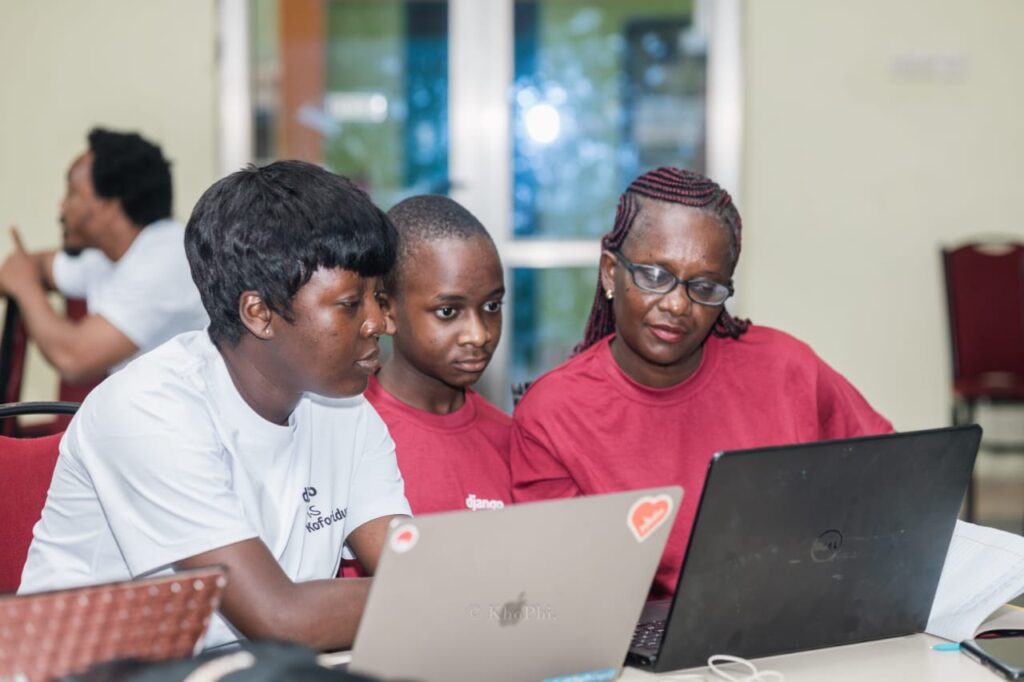 Theresa Seyram Agbenyegah working with two participants on laptops during a Django coding workshop.
