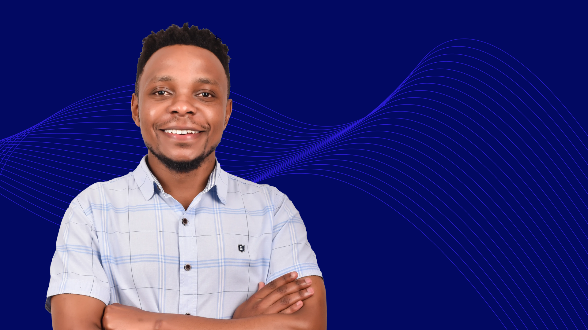Young man in blue and white short-sleeve shirt with crossed arms, looking at the camera, in front of a dark blue background